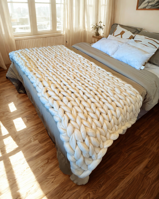 Pie de cama de lana natural con borlas.